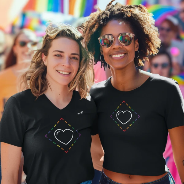 Two women celebrating Pride wearing ProudZone rainbow diamond t-shirts with colorful Pride flags behind them.