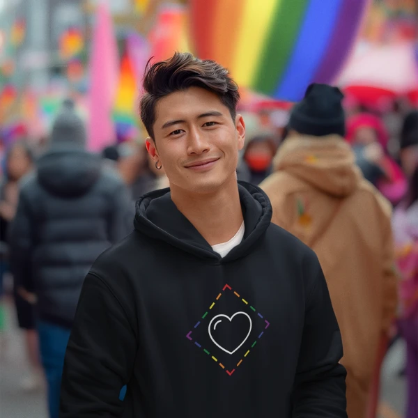 Young man wearing a ProudZone rainbow diamond hoodie at a Pride parade with rainbow flags in the background.